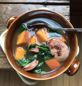 Kale, sausage and sweet potato soup in a brown bowl