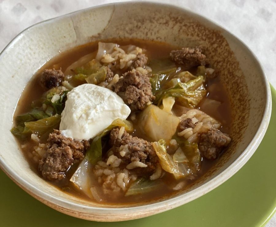 A bowl of soup with beef, cabbage and lettuce garnished with a dollop of sour cream
